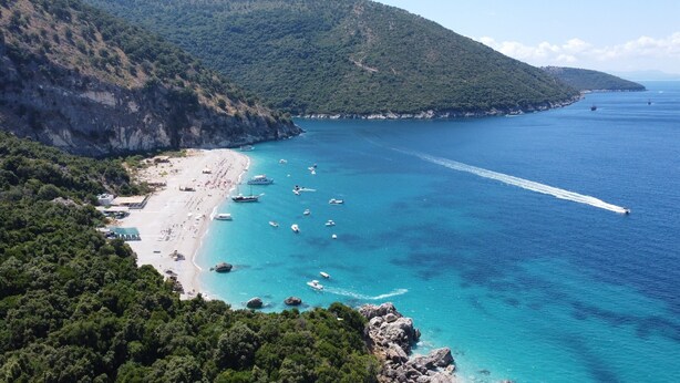 Une vue côtière avec une plage, des bateaux et une chaîne de montagnes en arrière-plan.