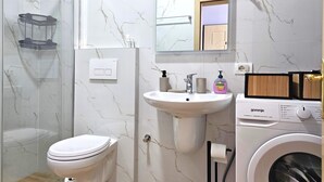 Une salle de bain équipée de toilettes, d’un lavabo, d’un miroir et d’un lave-linge.
