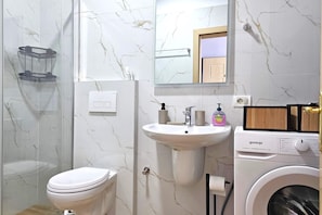 Un baño con inodoro, lavabo, espejo y lavadora.