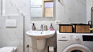 Une salle de bain avec un lavabo blanc, un miroir et un lave-linge.