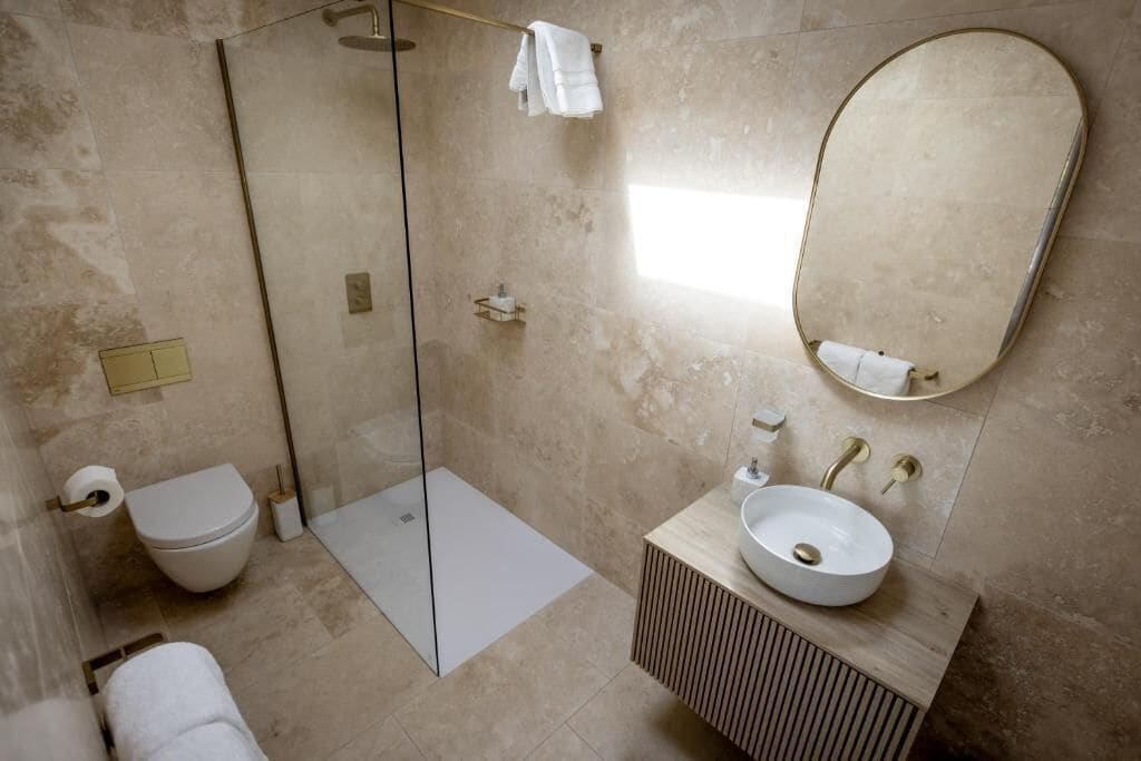 Een moderne badkamer met een douchecabine van glas, een toilet, een wastafel met spiegel en een handdoekrek.