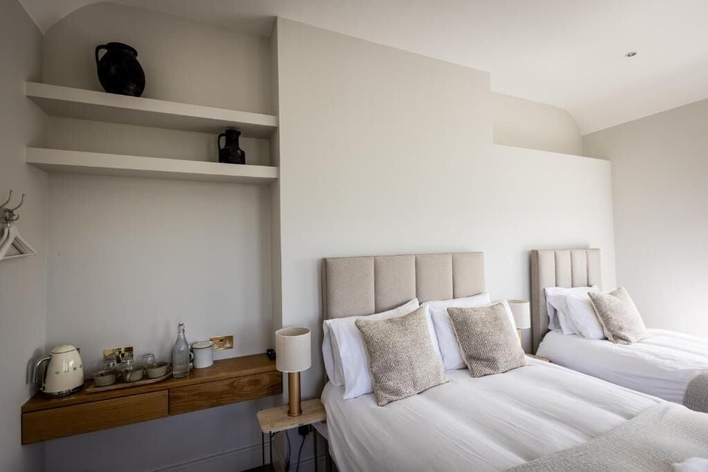 A bedroom with two beds, a nightstand, a shelf with decorative items, and a wall-mounted shelf.