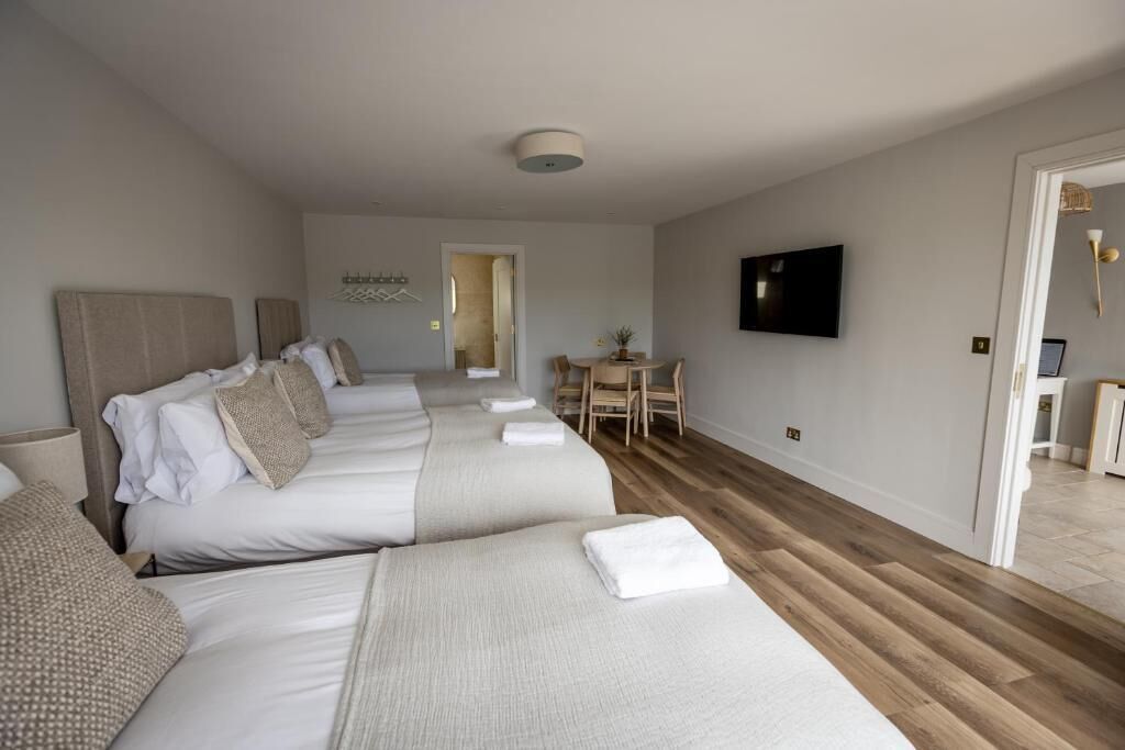 A hotel room with three beds, a TV, a small table, and a door leading to another room.