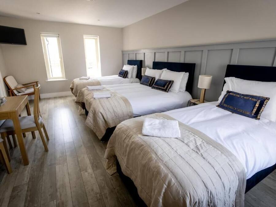 Ein Hotelzimmer mit drei Betten, einem Schreibtisch und Stühlen.