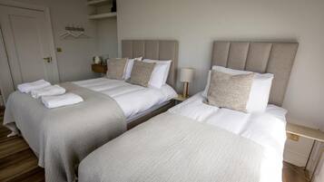 A hotel room with two beds, each with a headboard and pillows, a bedside table with a lamp, and a small shelf with items.