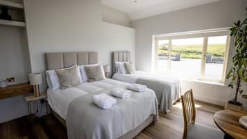 A hotel room with two beds, a wooden floor, a window with a view, and a small table with a chair.