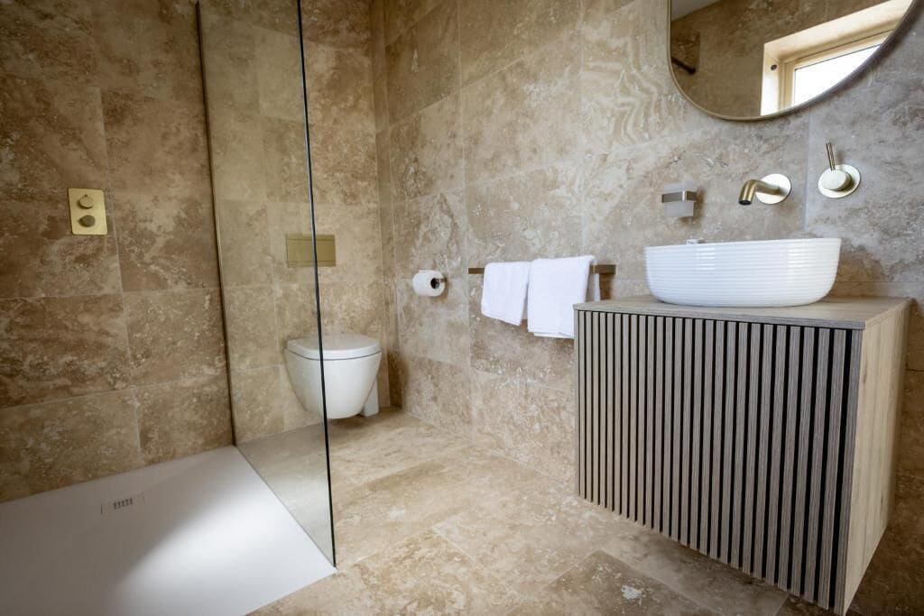 Un bagno moderno con doccia vetrata, un WC bianco, un lavabo a bacinella capiente e uno specchio sopra il lavabo.