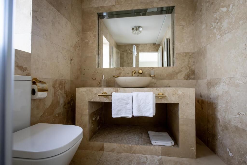 Un baño con un inodoro blanco, un lavamanos con espejo y un perchero para toallas.