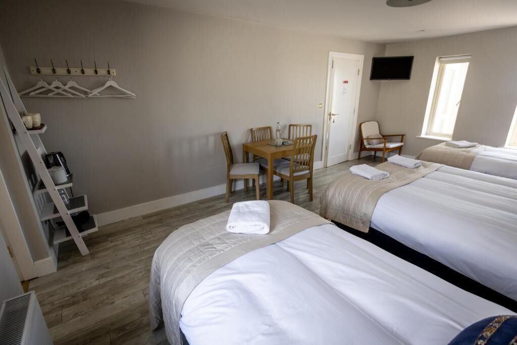 A hotel room with two beds, a desk with chairs, a TV, and a window.