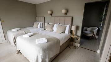 Habitación de hotel con dos camas, zona de estar y vistas al exterior.