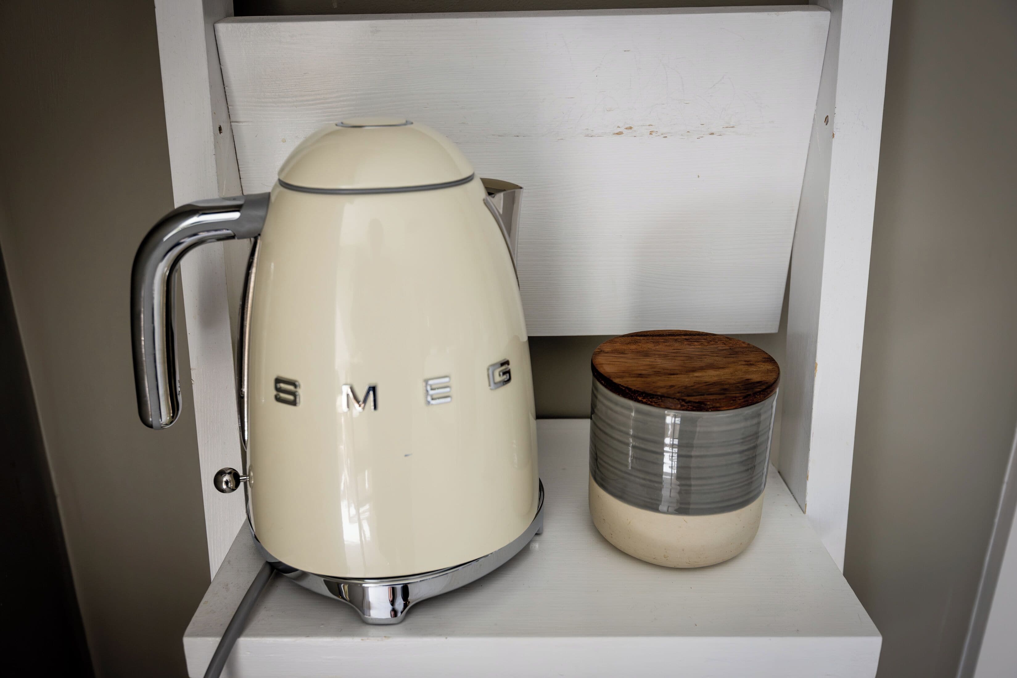 Una tetera vintage de Smeg y una taza de cerámica sobre un estante blanco.