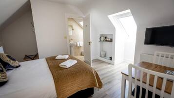 Une chambre à coucher avec un lit, un bureau, une chaise, un téléviseur et une fenêtre de toit.
