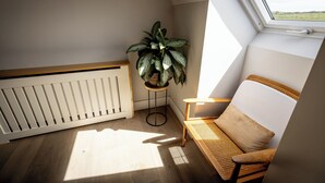A cozy room with a sloped ceiling, a radiator, a wooden bench, a potted plant, and a window with a view of the countryside. - Coastal View House (Doolin)