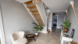A modern living room with a white armchair, a small round table, a potted plant, and a staircase with wooden steps. - Coastal View House (Doolin)