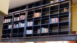 Eine moderne Küche mit eingebautem Bücherregal über der Arbeitsplatte, einem Edelstahl-Spülbecken und einem Wasserkocher auf der Theke.
