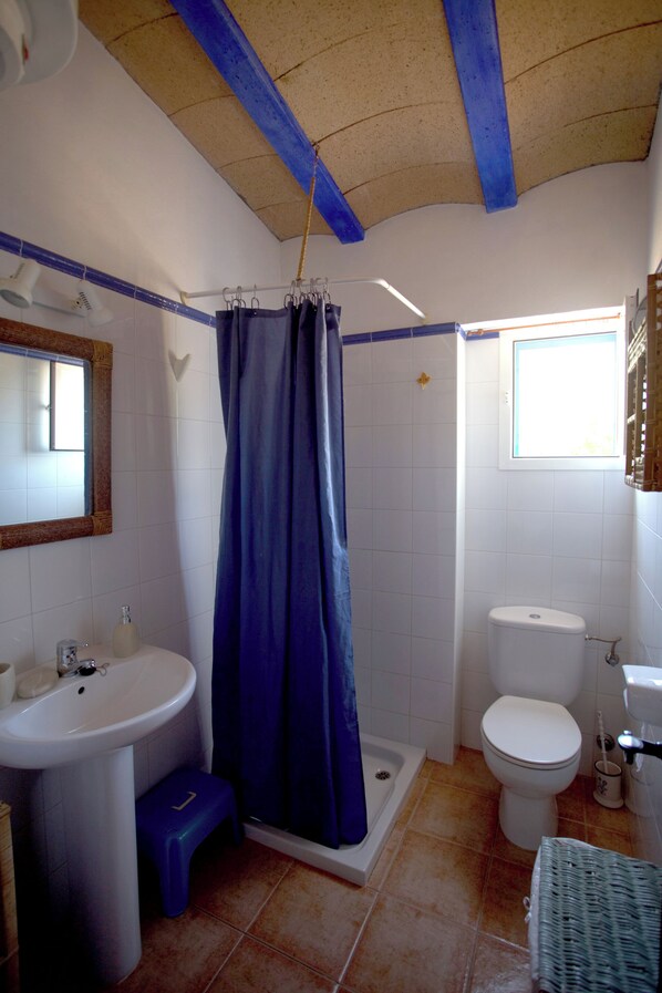 A bathroom with a white sink, blue shower curtain, white toilet, and a window providing natural light.