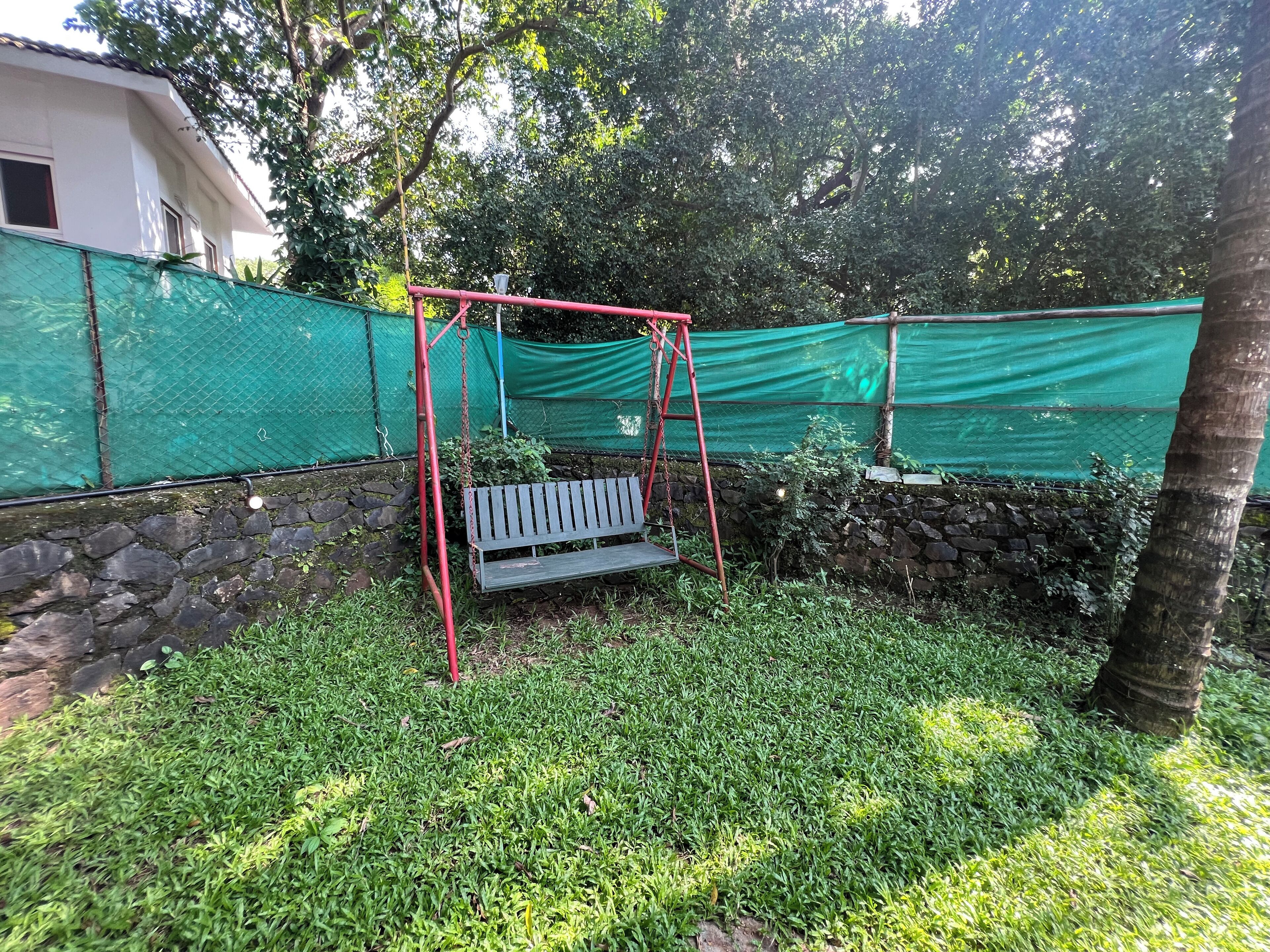 Un jardín con un columpio, un muro de piedra y una malla verde.