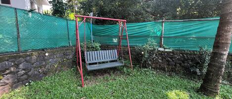 Un jardín con un columpio, un muro de piedra y una malla verde.