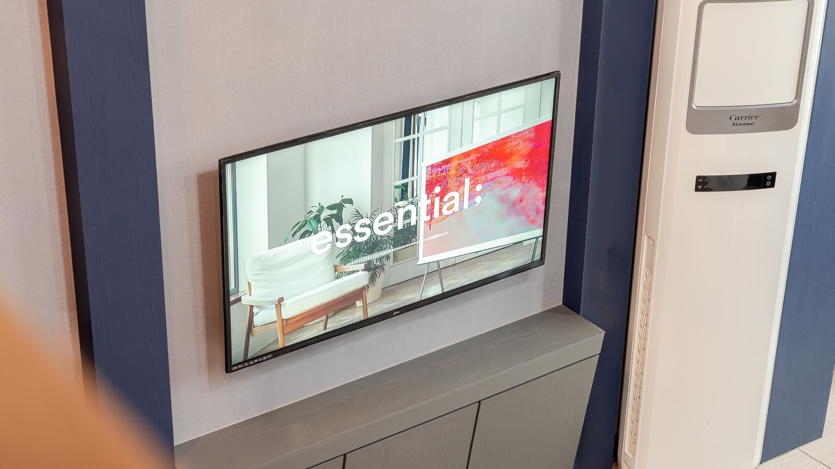 Un téléviseur à écran plat fixé au mur, avec un panneau gris en dessous.