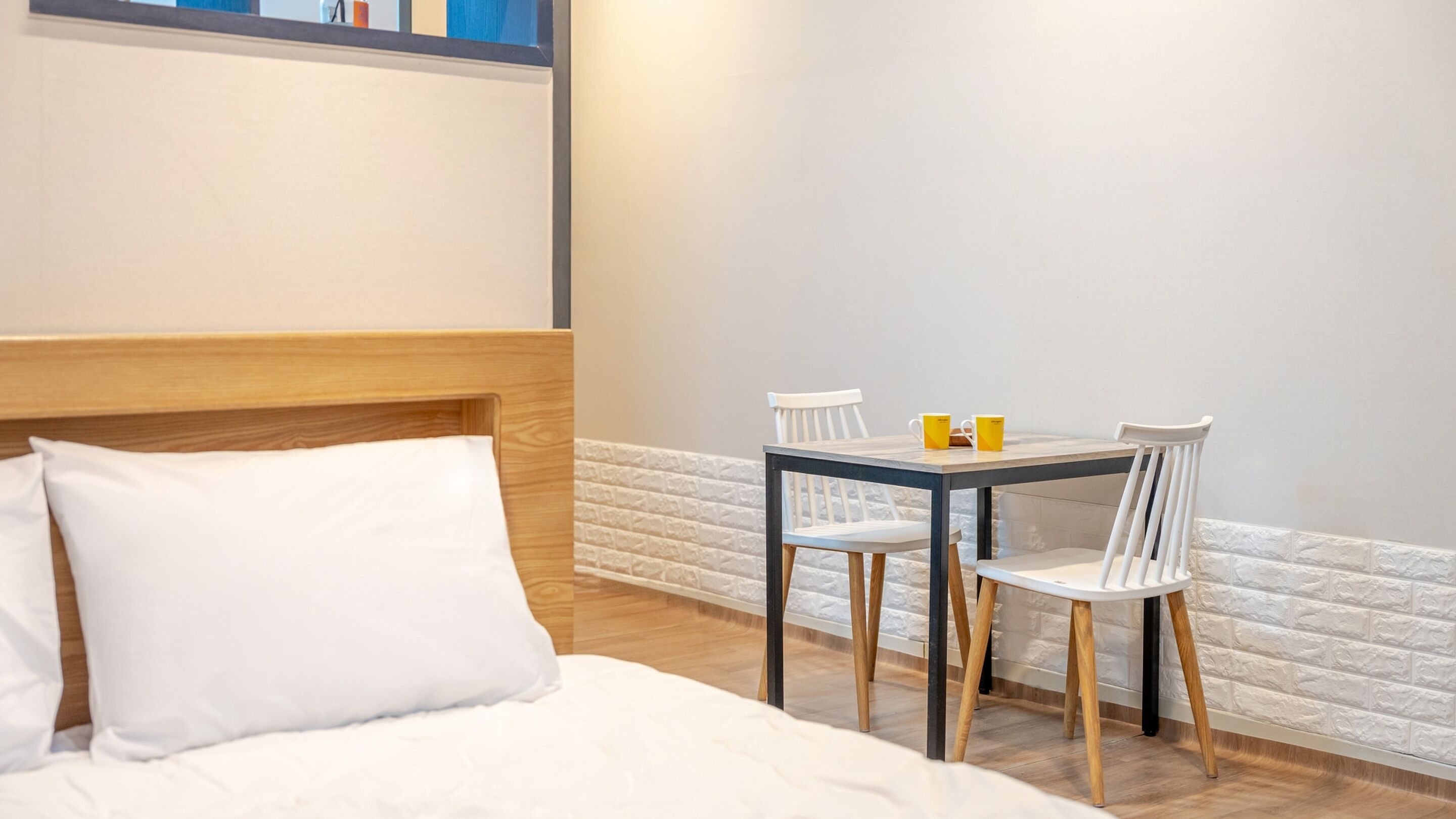 Une chambre d’hôtel avec un lit, une petite table et deux chaises, et un mur décoré d’un motif en briques blanches.
