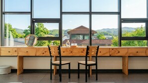A room with a large window, two wooden chairs, a desk, and a view of a building and mountains. - Gyeongju Bomun Arno Pool Villa (Gyeongju)