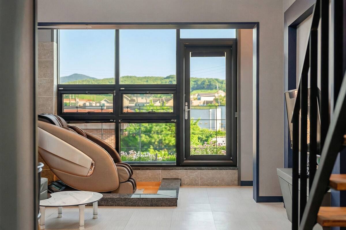 A modern room with a large window, a massage chair, a small table, and a staircase.