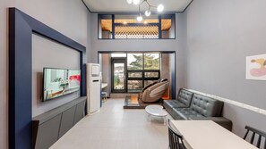 A modern living room with a sofa, a dining table, and a TV. There is a large window with a view of the outdoors. - Gyeongju Bomun Arno Pool Villa (Gyeongju)
