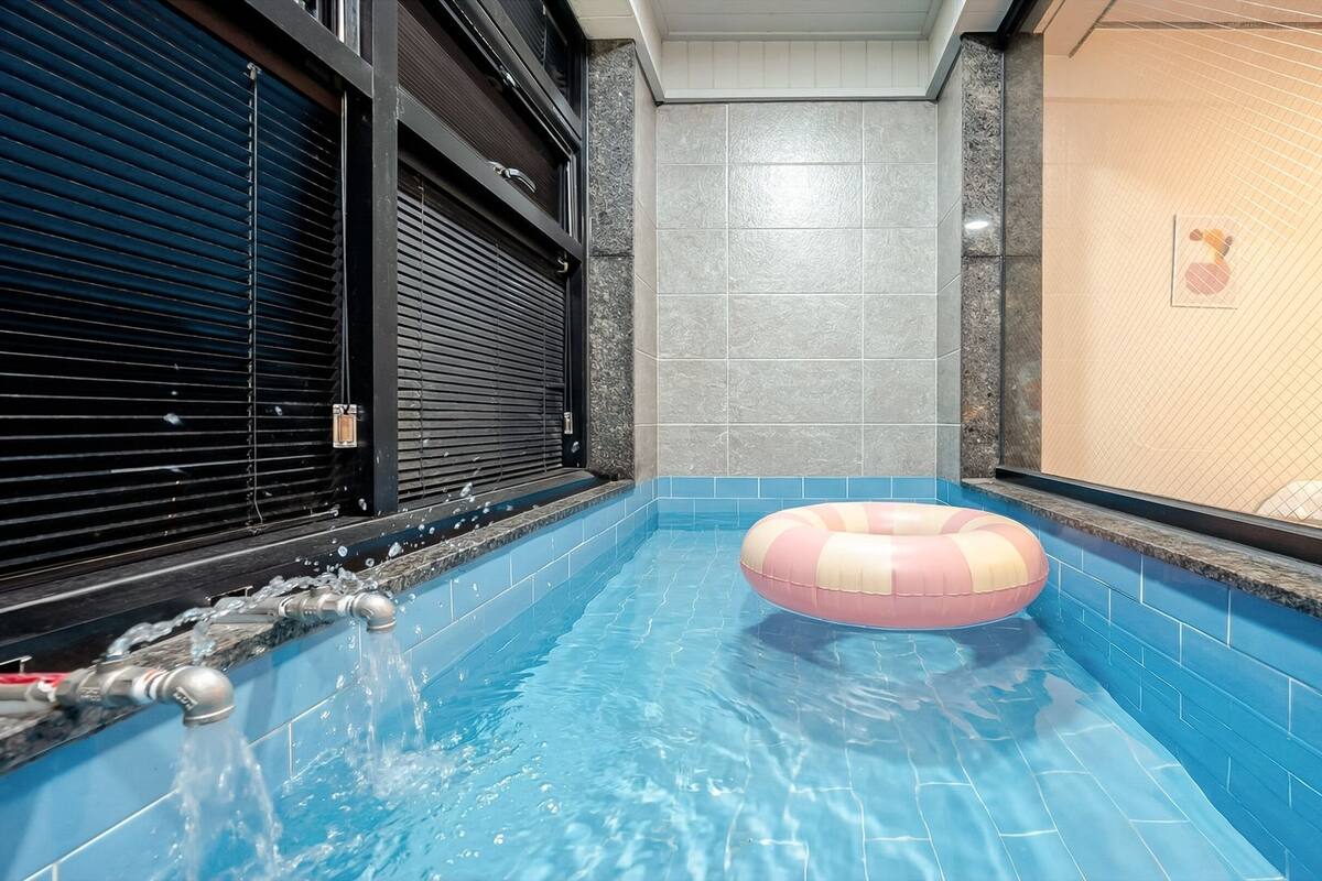 A swimming pool with a pink and white inflatable ring, tiled walls, and a closed shutter on the left.