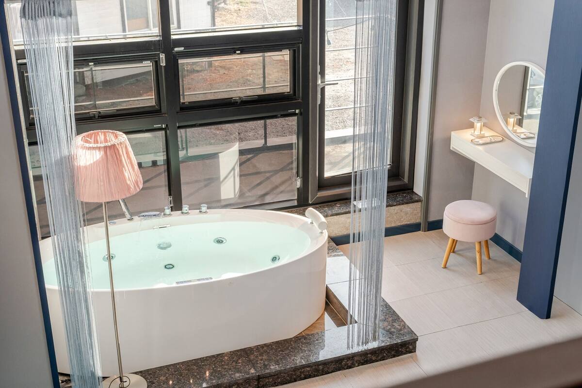 A bathroom with a large bathtub, a vanity with a mirror, and a stool.