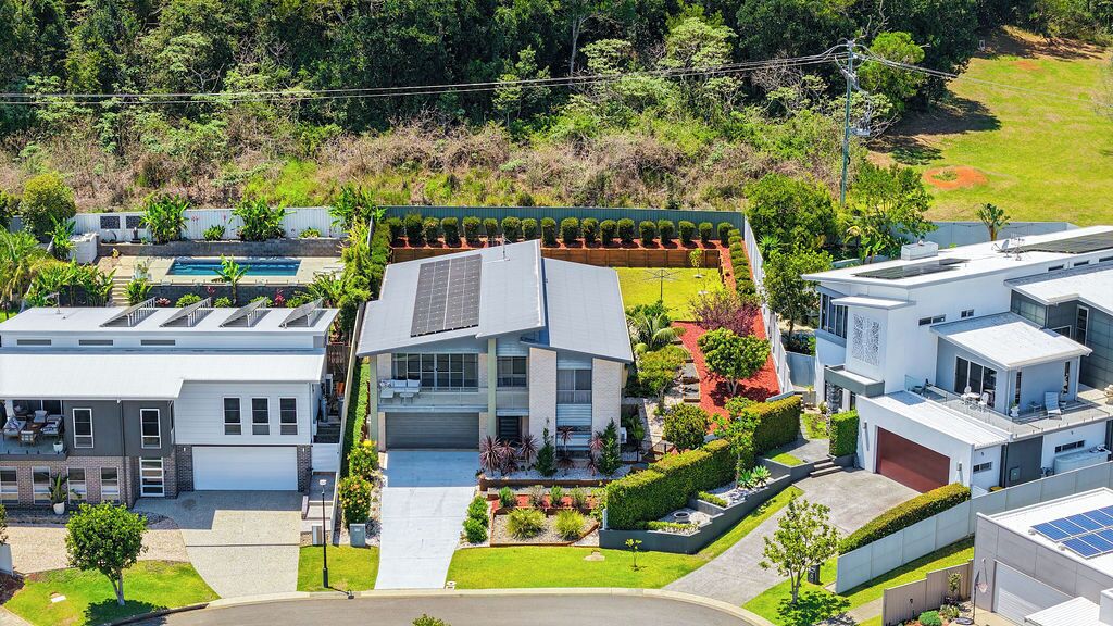 Un immeuble résidentiel moderne doté d’un toit en pente, de panneaux solaires et d’un jardin bien entretenu, agrémenté de diverses plantes et d’une piscine.