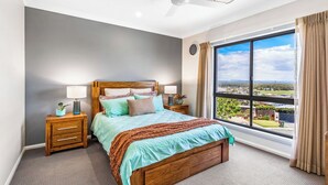 Ein Schlafzimmer mit großem Fenster, einem Bett mit Holz Kopfteil, zwei Nachttischen mit Lampen und Blick auf eine Landschaft.