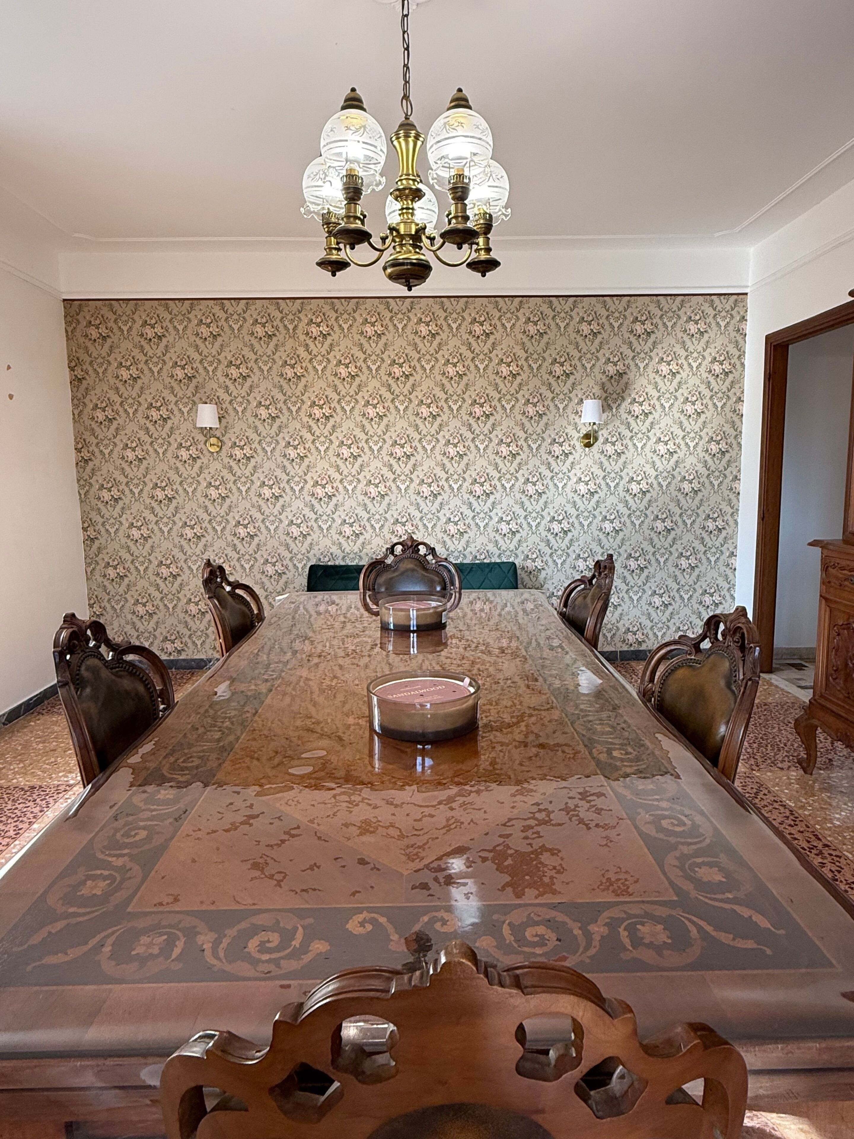 A long dining table with ornate chairs, a chandelier, and patterned wallpaper.