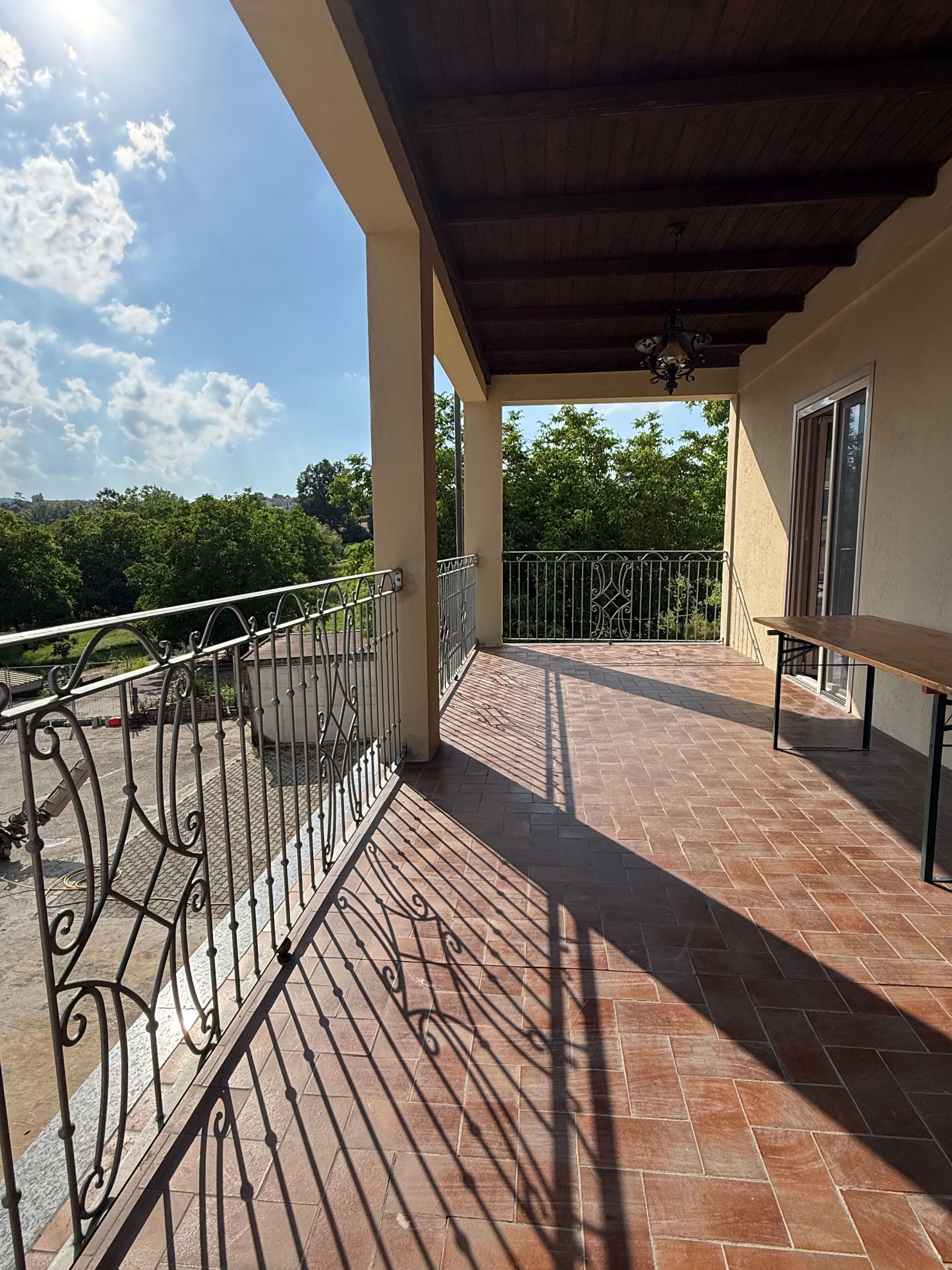 Un balcon extérieur abrité, doté d’un sol carrelé, d’une rambarde en métal et d’un banc.