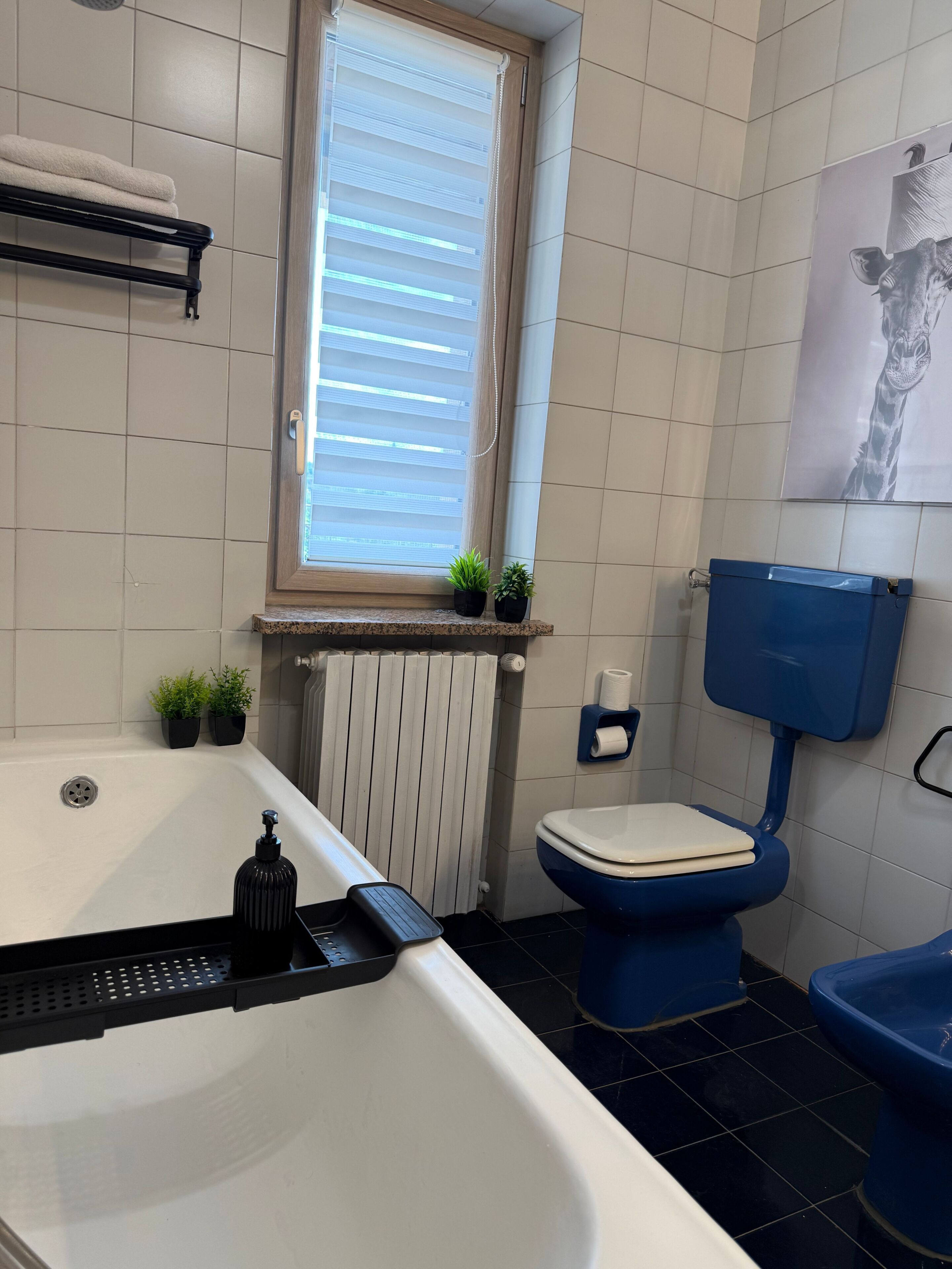 Ein Badezimmer mit Badewanne, Toilette, Heizkörper und einem Fenster mit Jalousien.
