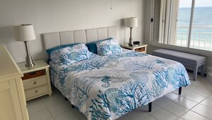 Ein Schlafzimmer mit einem Bett, zwei Nachttischen, einer Bank und Meerblick.
