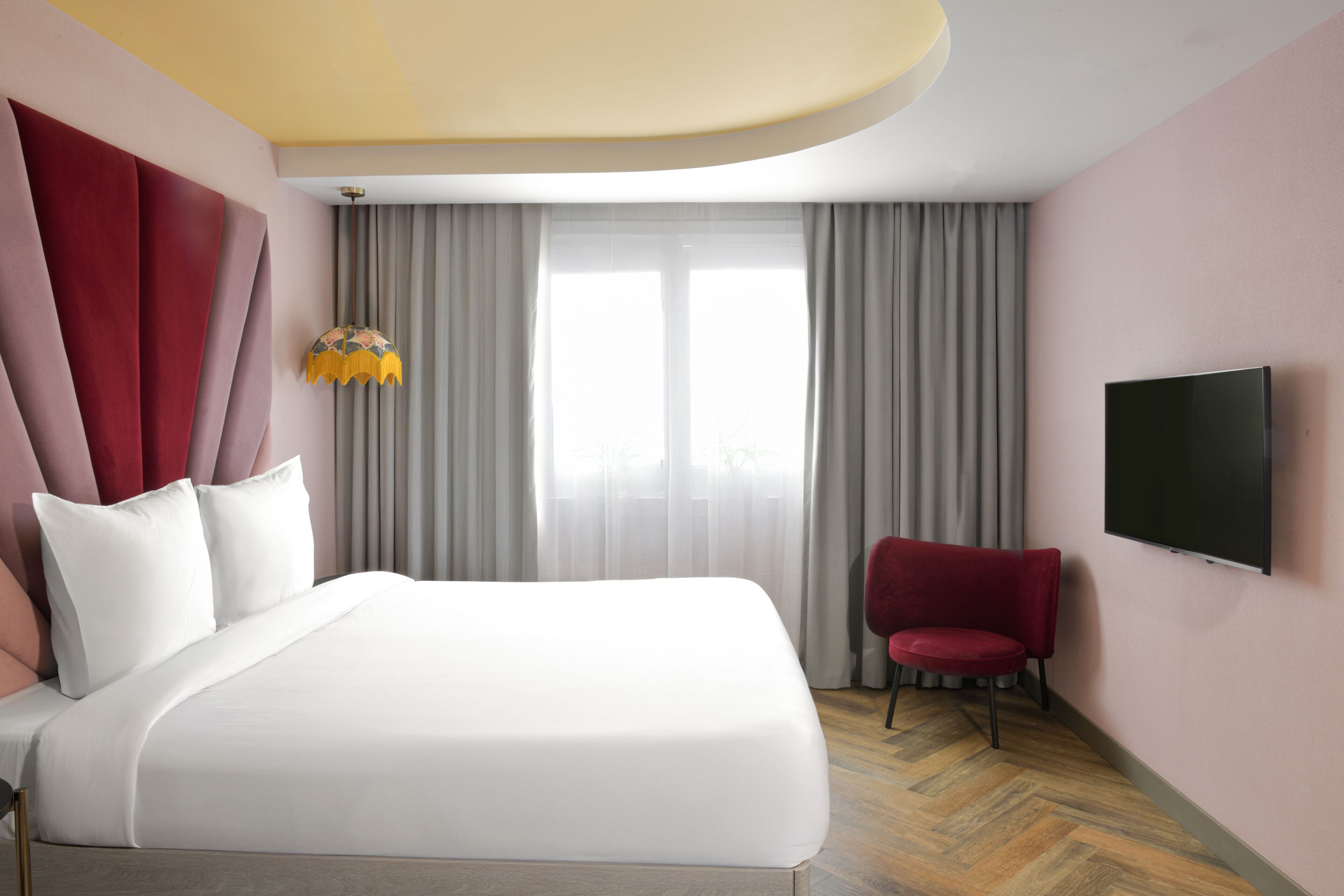 A hotel room with a large bed, a red chair, a flat-screen TV, and a window with curtains.