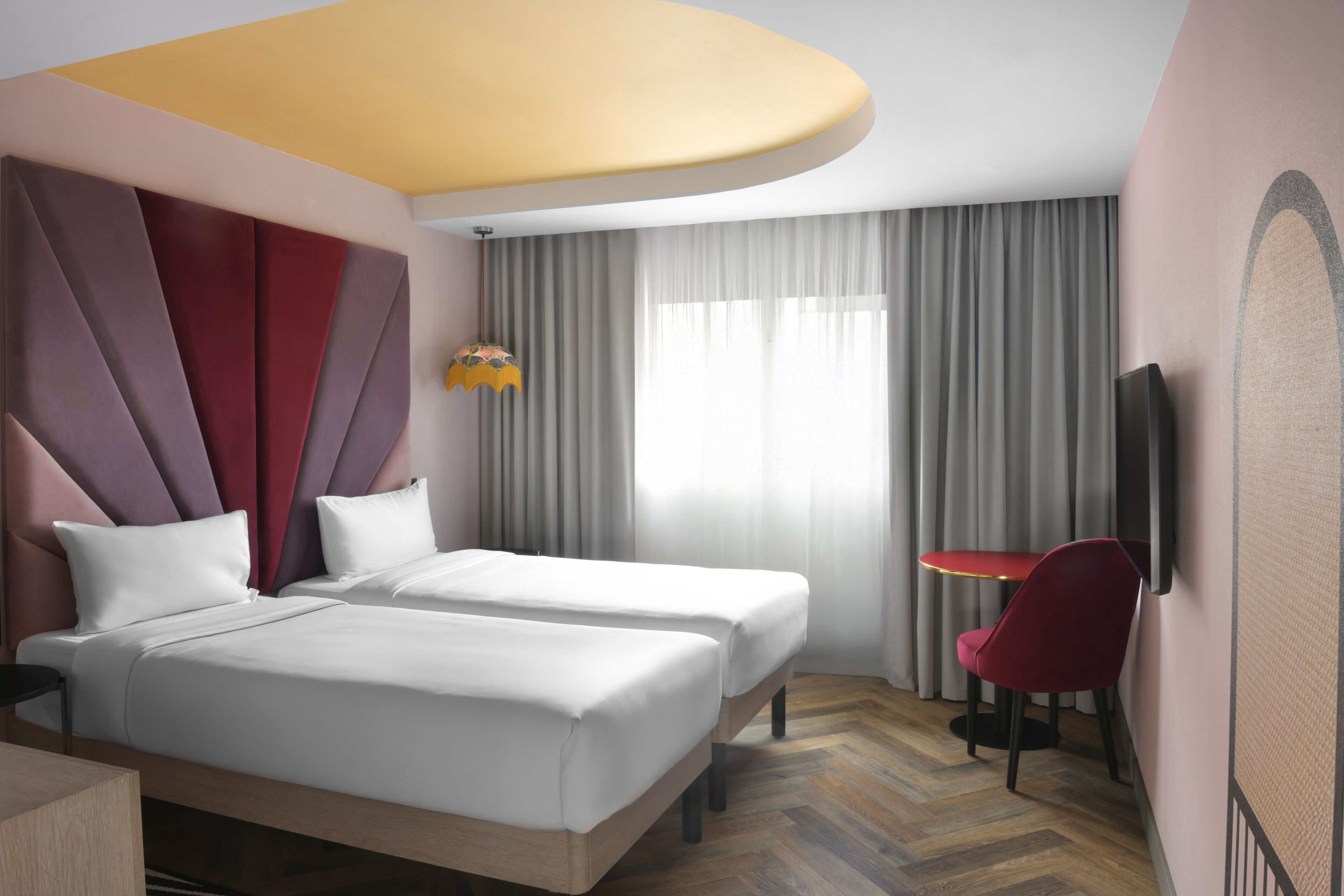 A hotel room with two beds, a desk, a chair, a TV, and a large window with curtains.