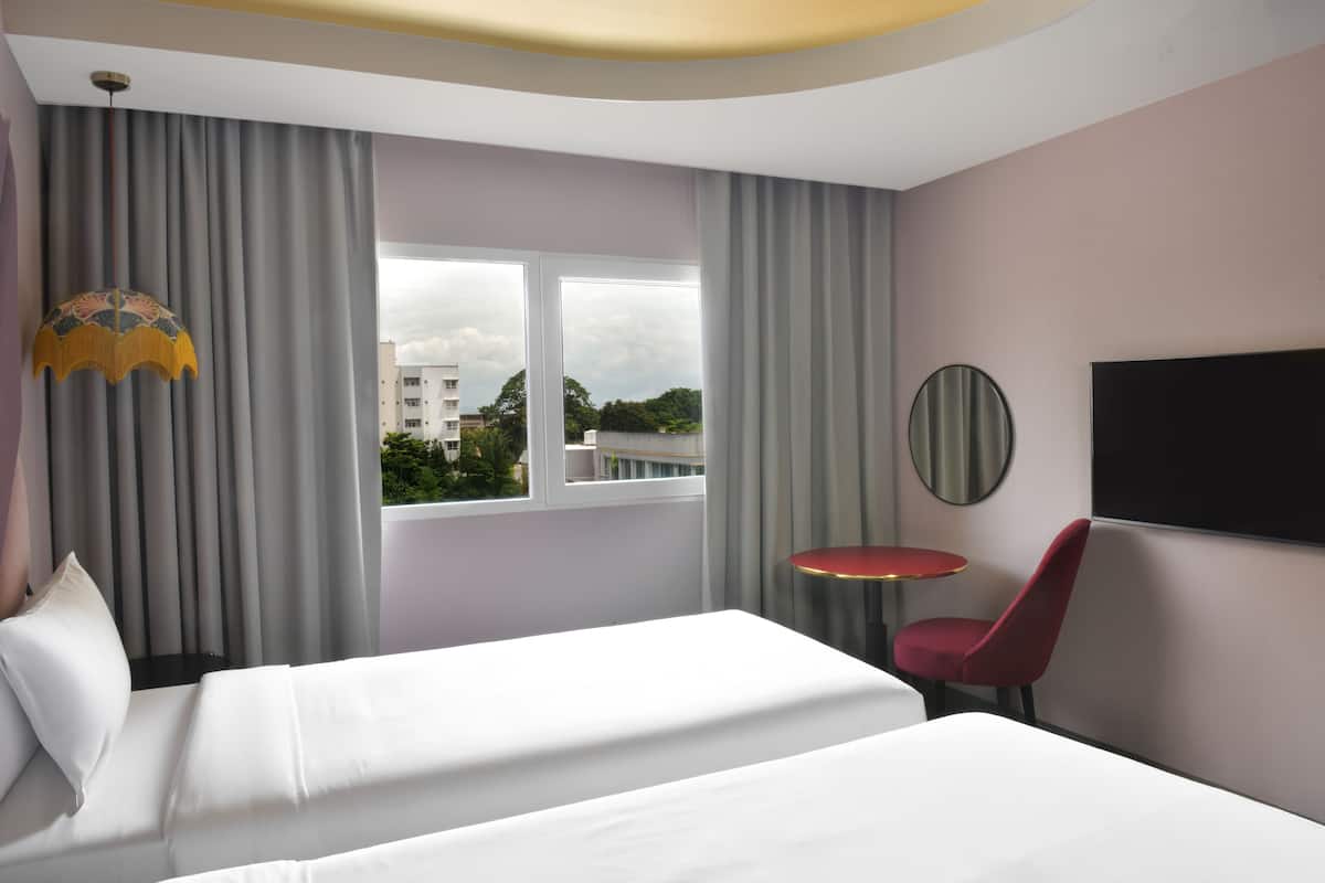 A hotel room with a bed, a red chair, a round table, a TV, and a window with curtains.