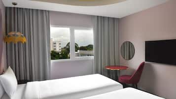 A hotel room with a bed, a red chair, a round table, a TV, and a window with curtains.