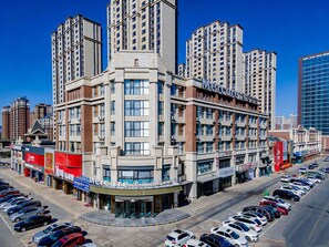 A multi-story hotel with a prominent entrance, a parking lot, and surrounding high-rise buildings. - Mercure Huhhot Economic Zone (Hohhot)