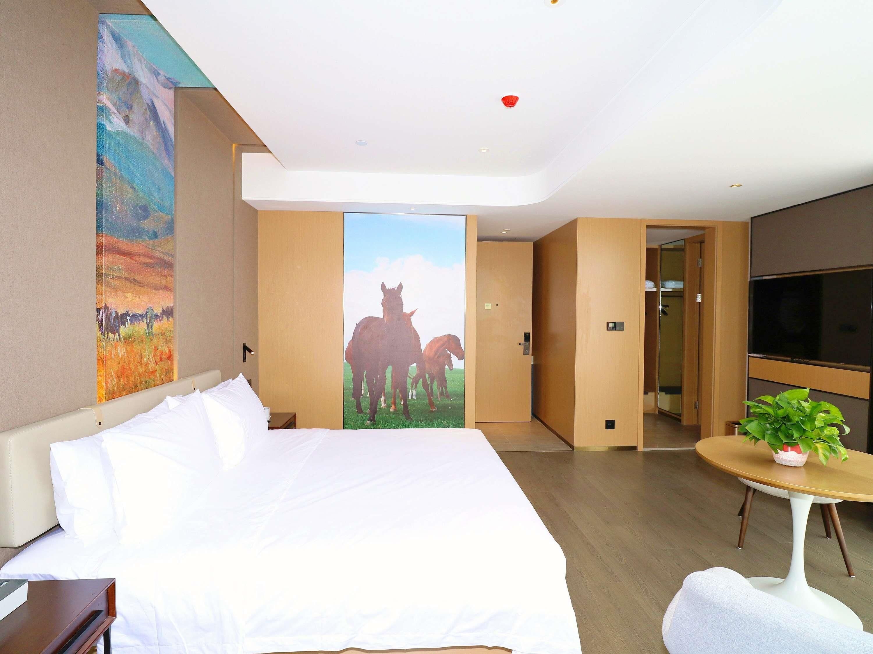 Habitación de hotel con una cama grande, un cuadro de caballos, un televisor y una pequeña mesa con una planta.