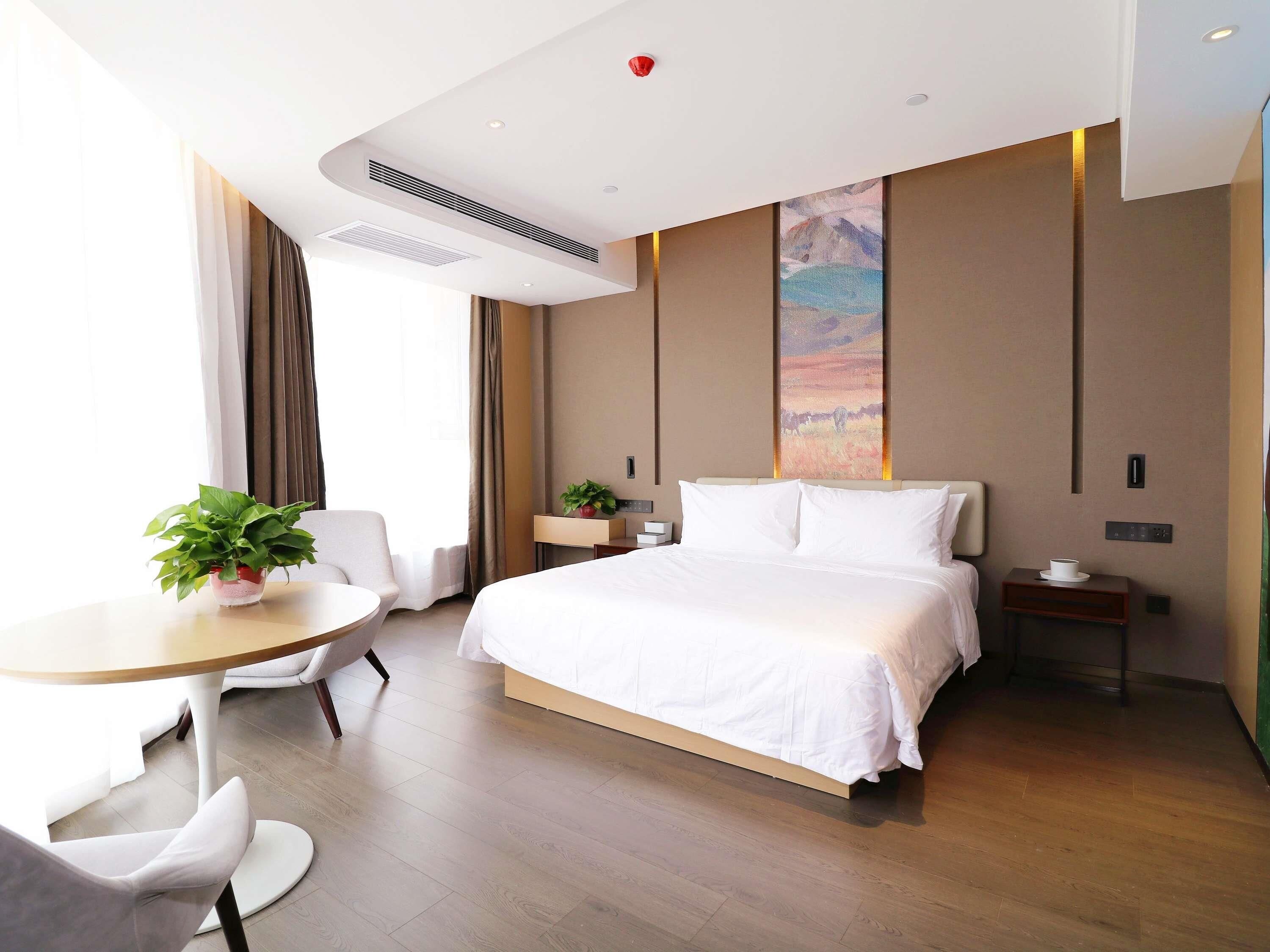 Una habitación de hotel con cama, mesita de noche, silla y una pequeña mesa con una planta.