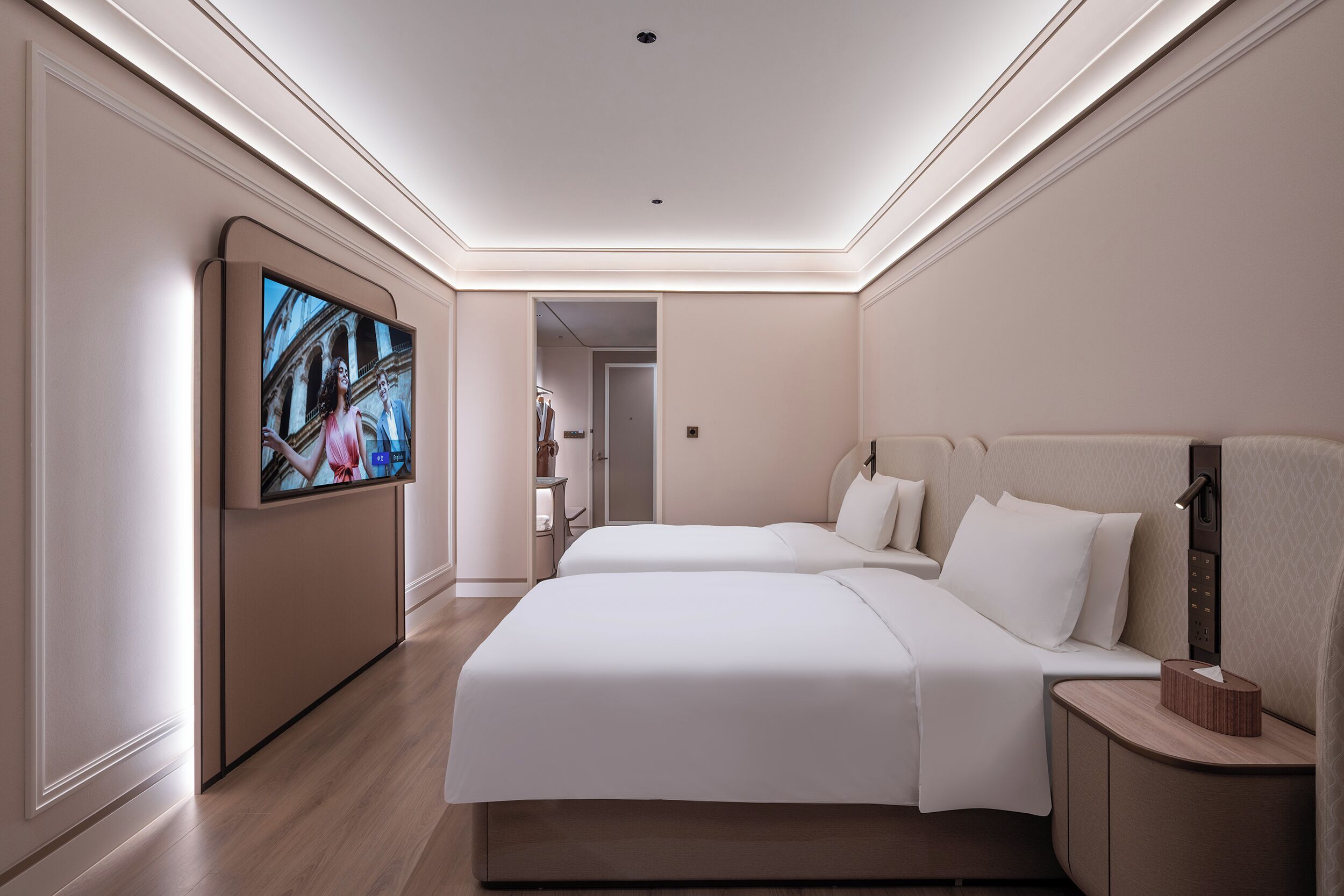 Habitación de hotel con dos camas, un televisor montado en la pared y una mesita de noche con lámpara.