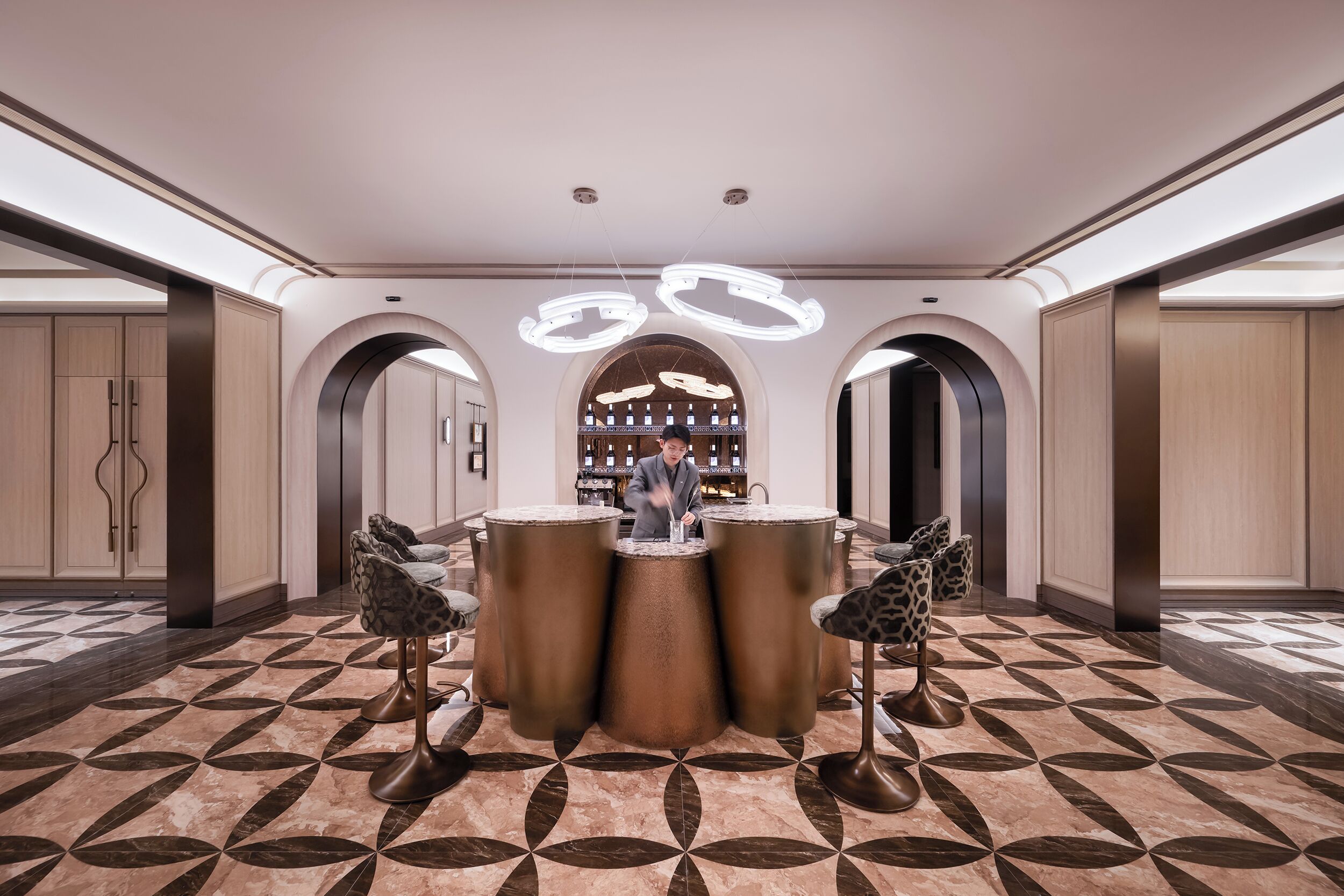 Um lobby moderno com área de bar central, portas em arco e piso estampado.
