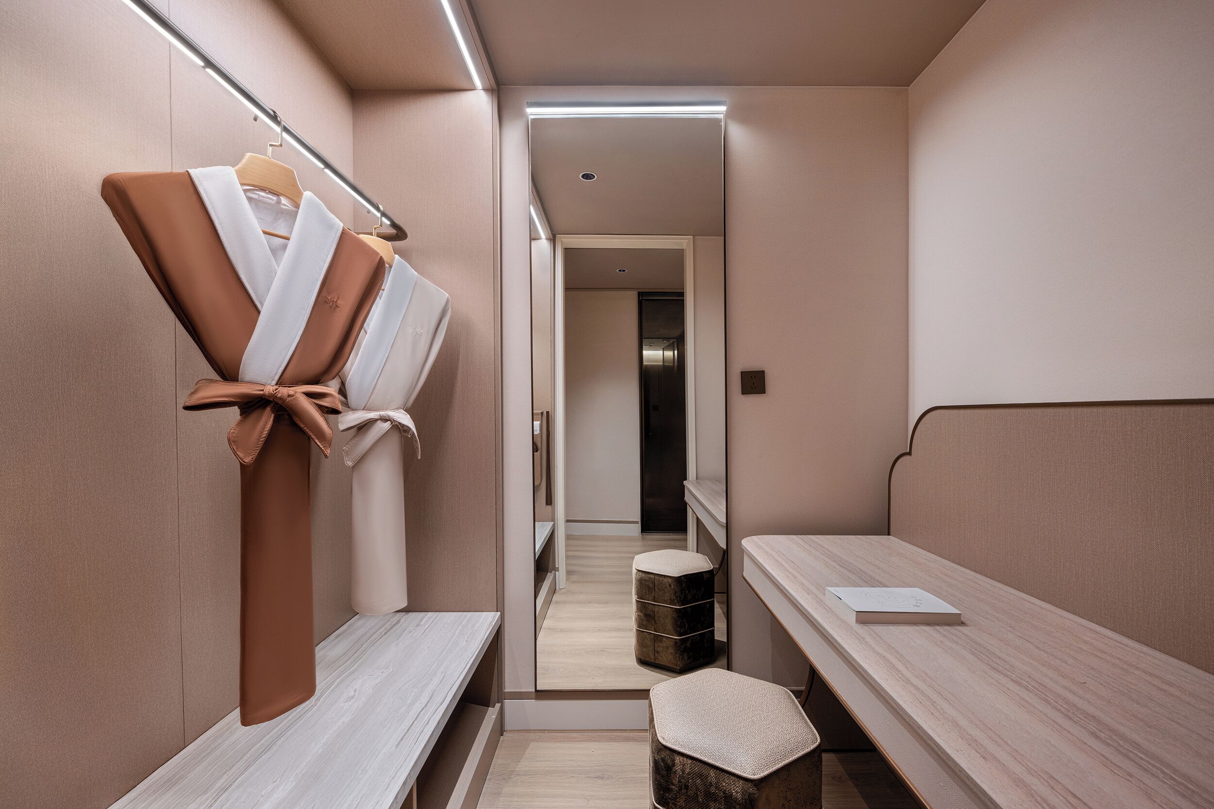 A hotel room with a bed, a bench, a mirror, and a small stool.