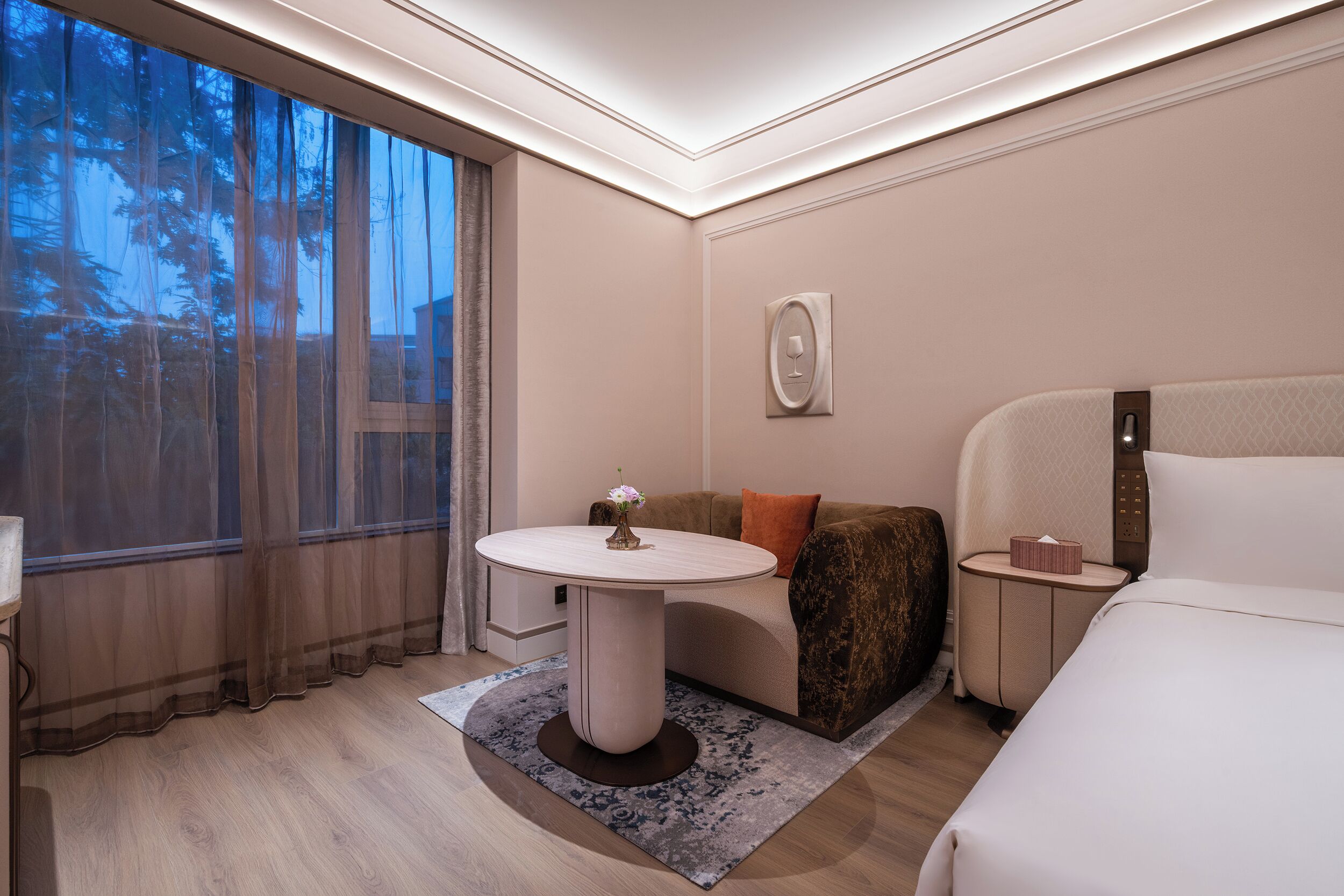 Une chambre d’hôtel avec un lit, une table ronde, un canapé et une fenêtre avec des rideaux.