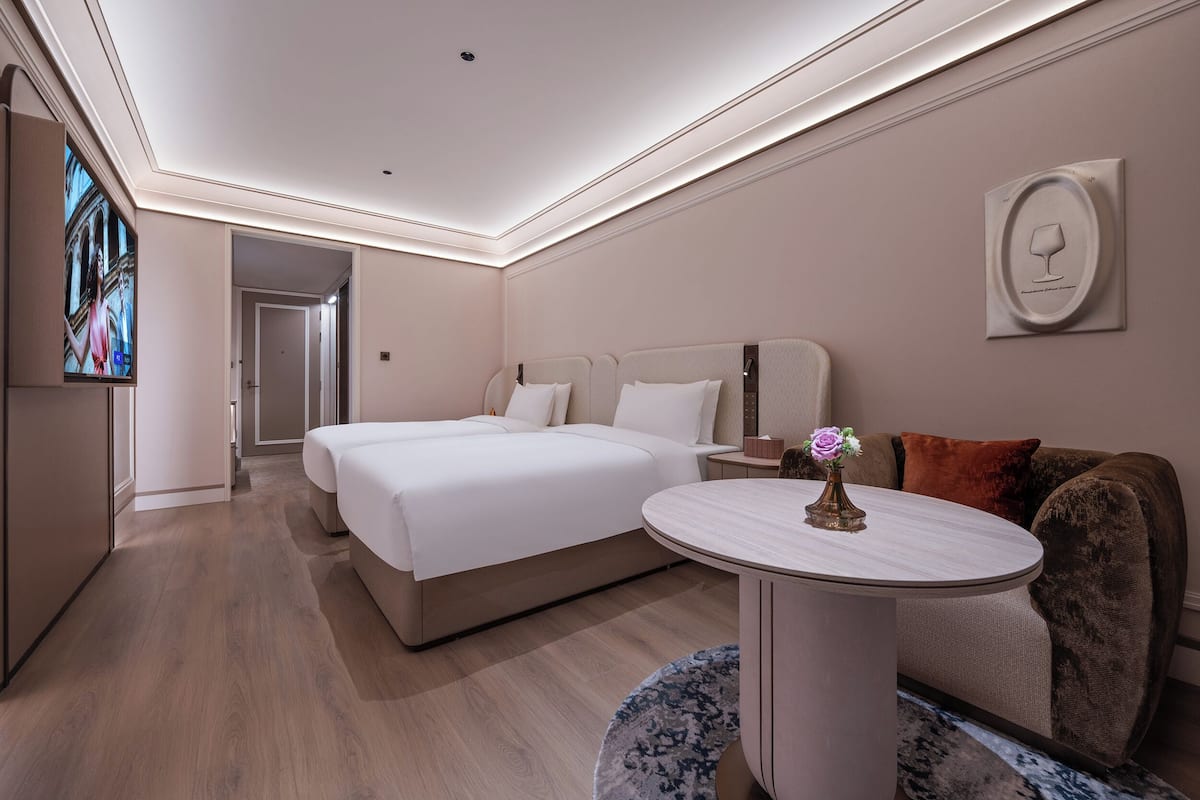 A hotel room with a bed, a round table with a vase, a sofa, and a TV on the wall.