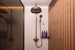 Una ducha con cabezal de ducha de mano y otro fijo en la pared, un perchero y un estante con artículos de aseo.