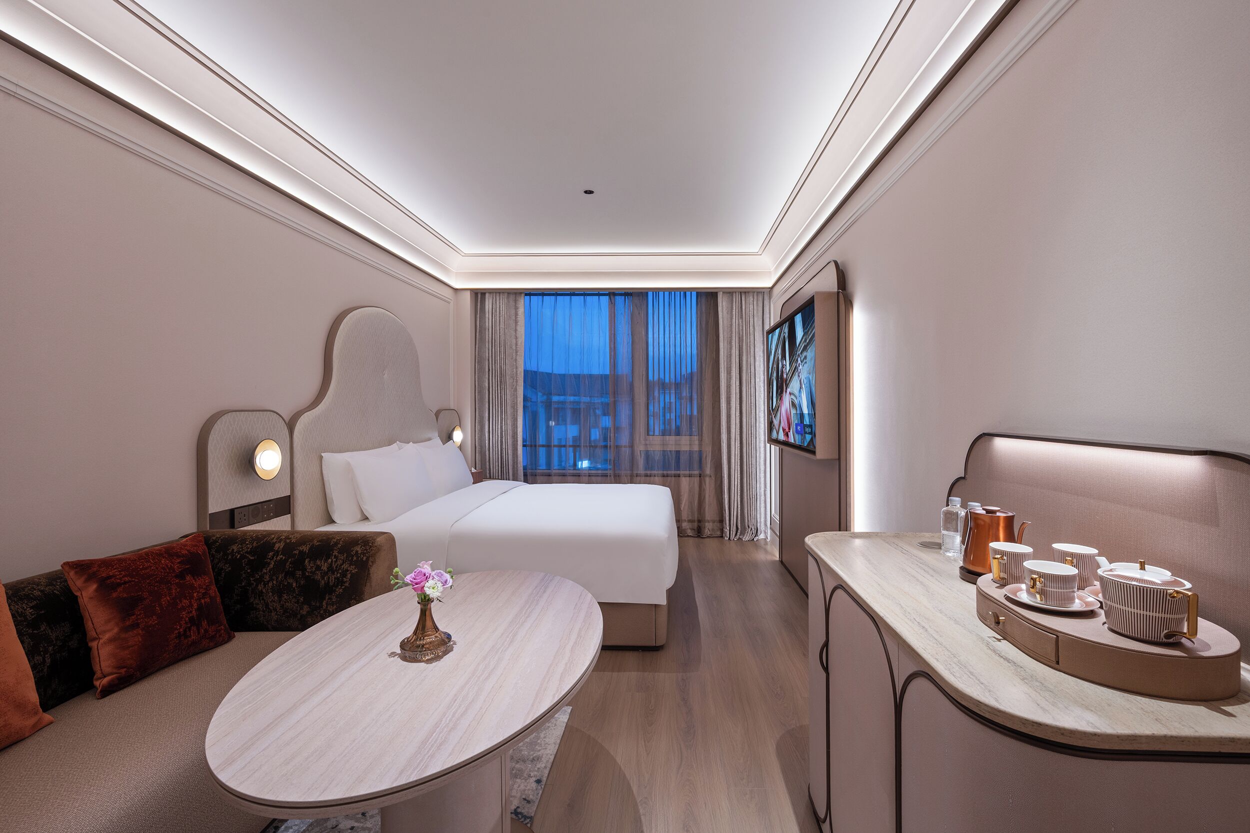 A modern hotel room with a bed, seating area, and a dining table.