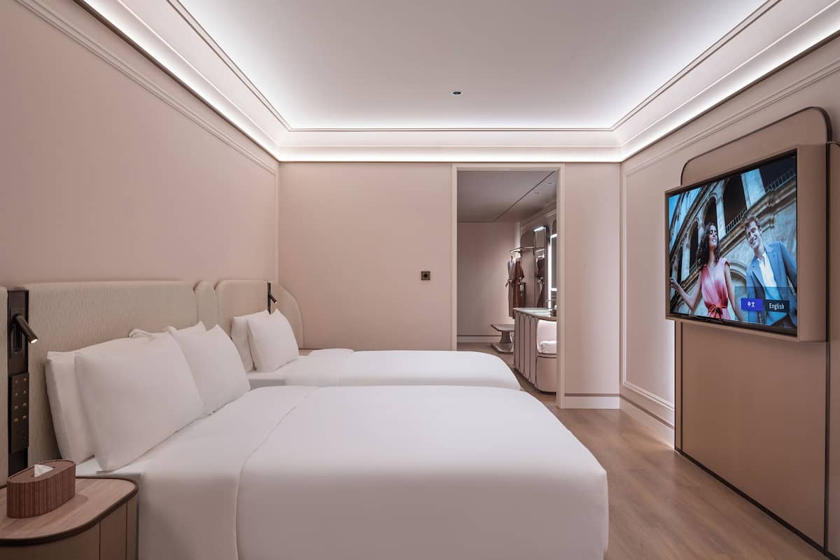 A hotel room with two beds, a TV, a bedside table, and a mirror.